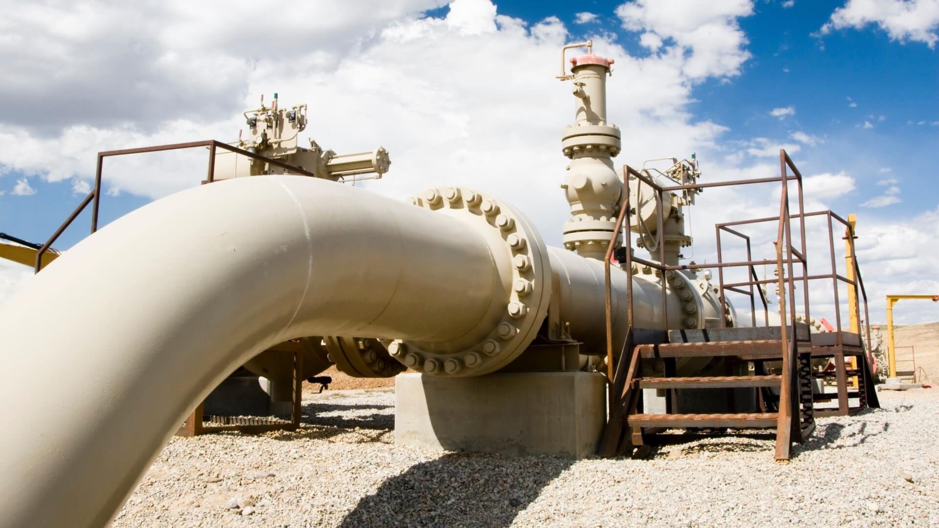 Close up of gas pipeline, valves and inspection ladders, with blue sky and clouds above