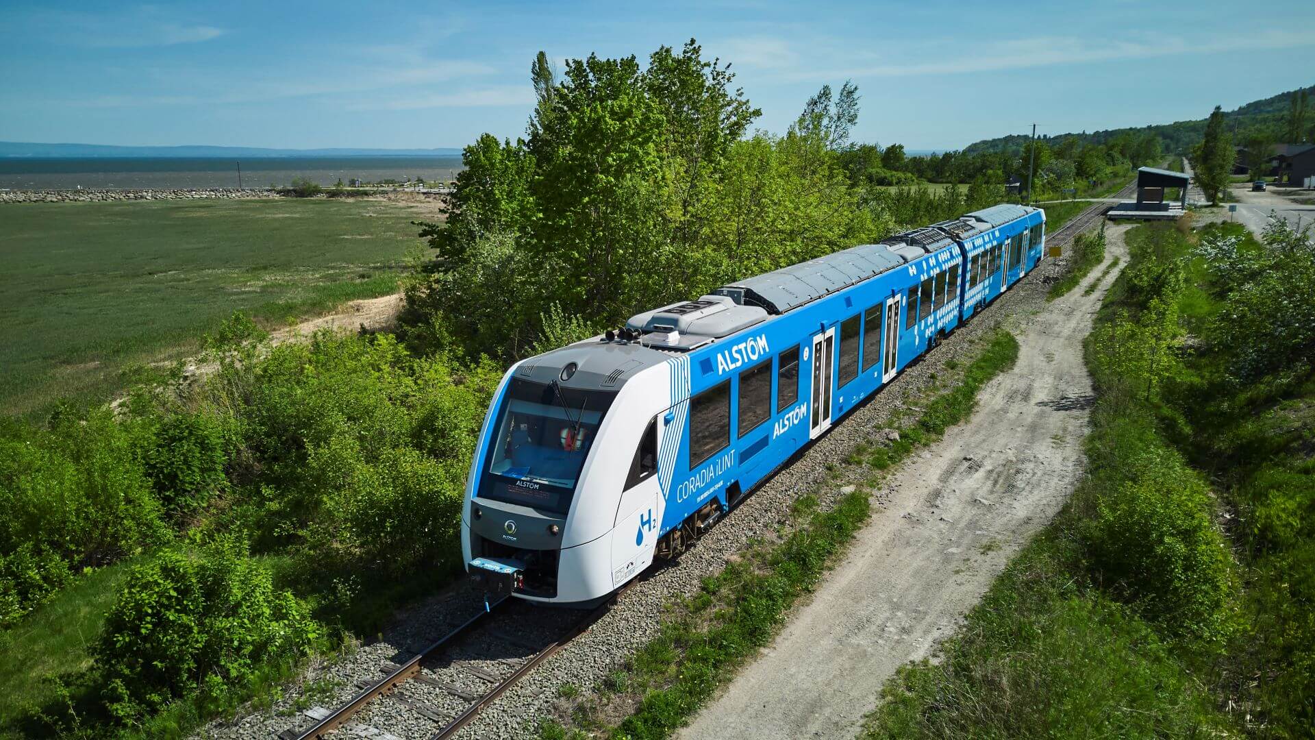 Blue and white hydrogren powered train travelling diagonally across picture right to left, through green countryside