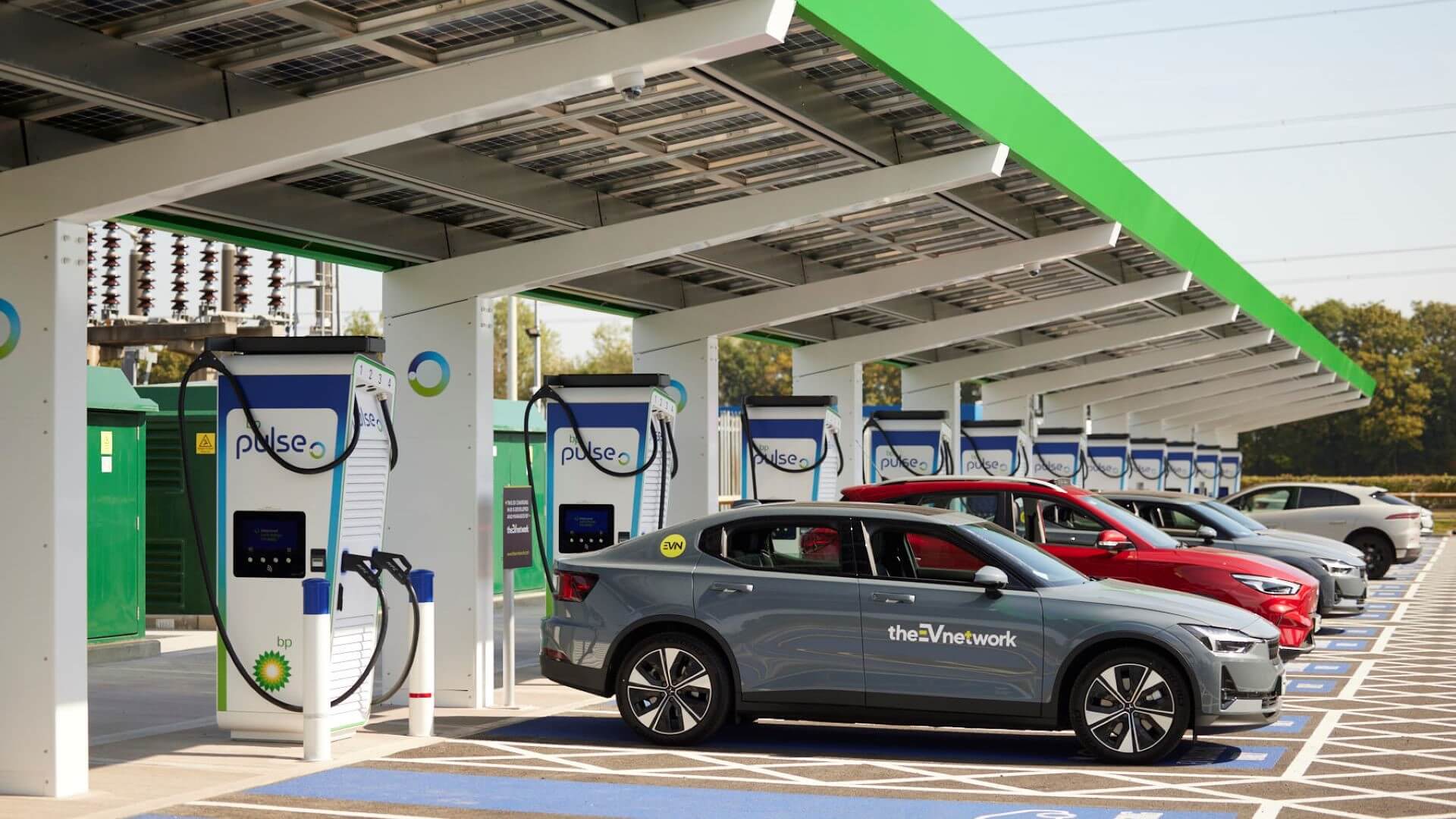 Row of electric powered cars lined up and repowering at charging points under forecourt canopy