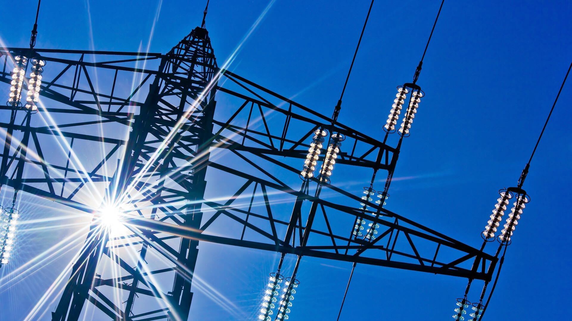 Looking skywards from base of electricity pylon, up through the metalwork to blue sky and sunburst 