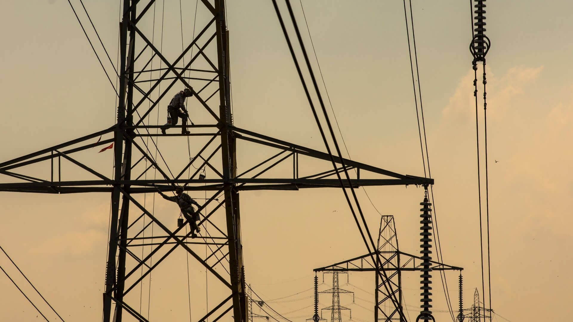 Row of pylons silhouetted against sunset, with two maintenance operators at top of first pylon