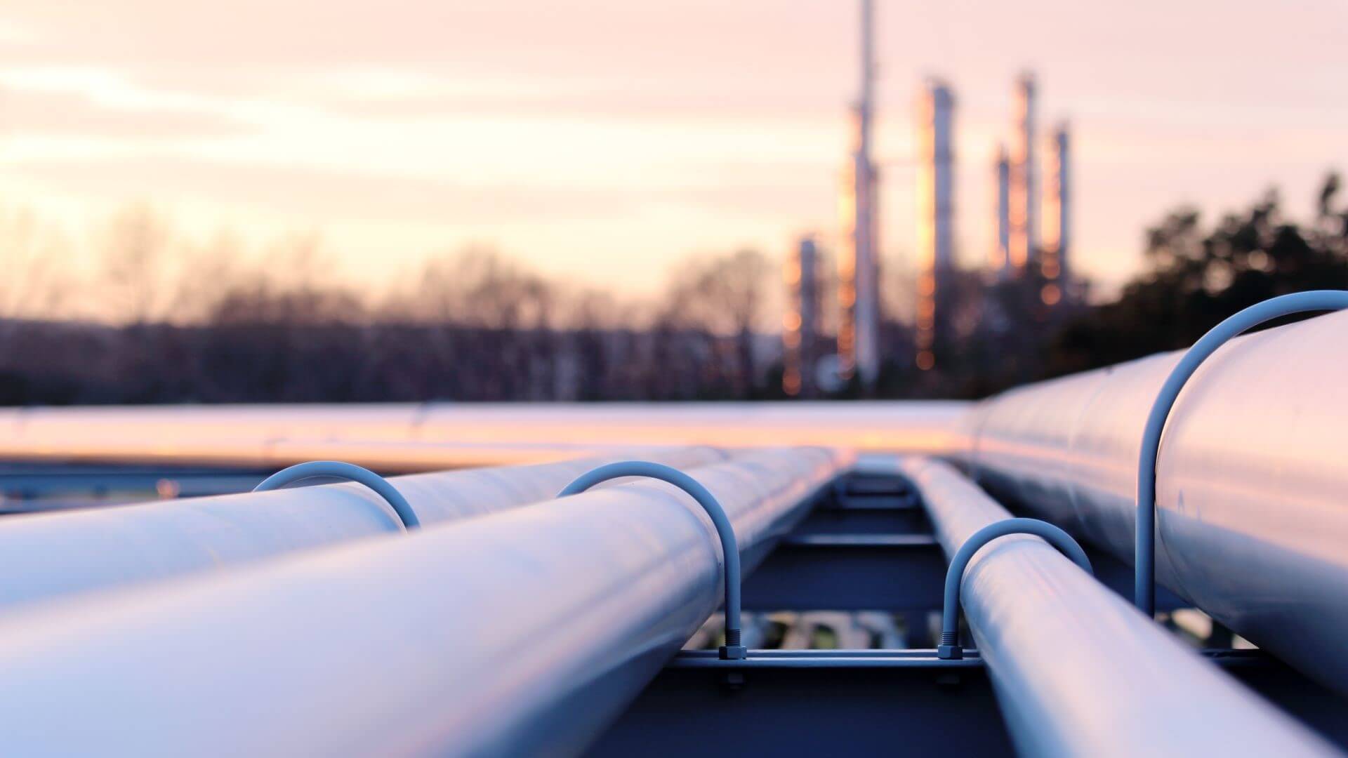 Close up of four pipelines extending from foreground to back right of photo, with blurred industry plant facilities in background