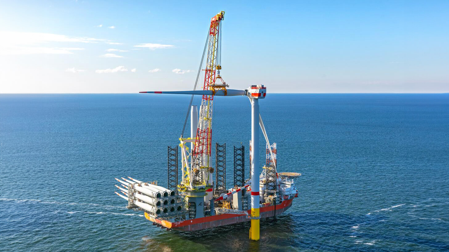Vessel crane installilng blade on a wind turbine in calm blue sea