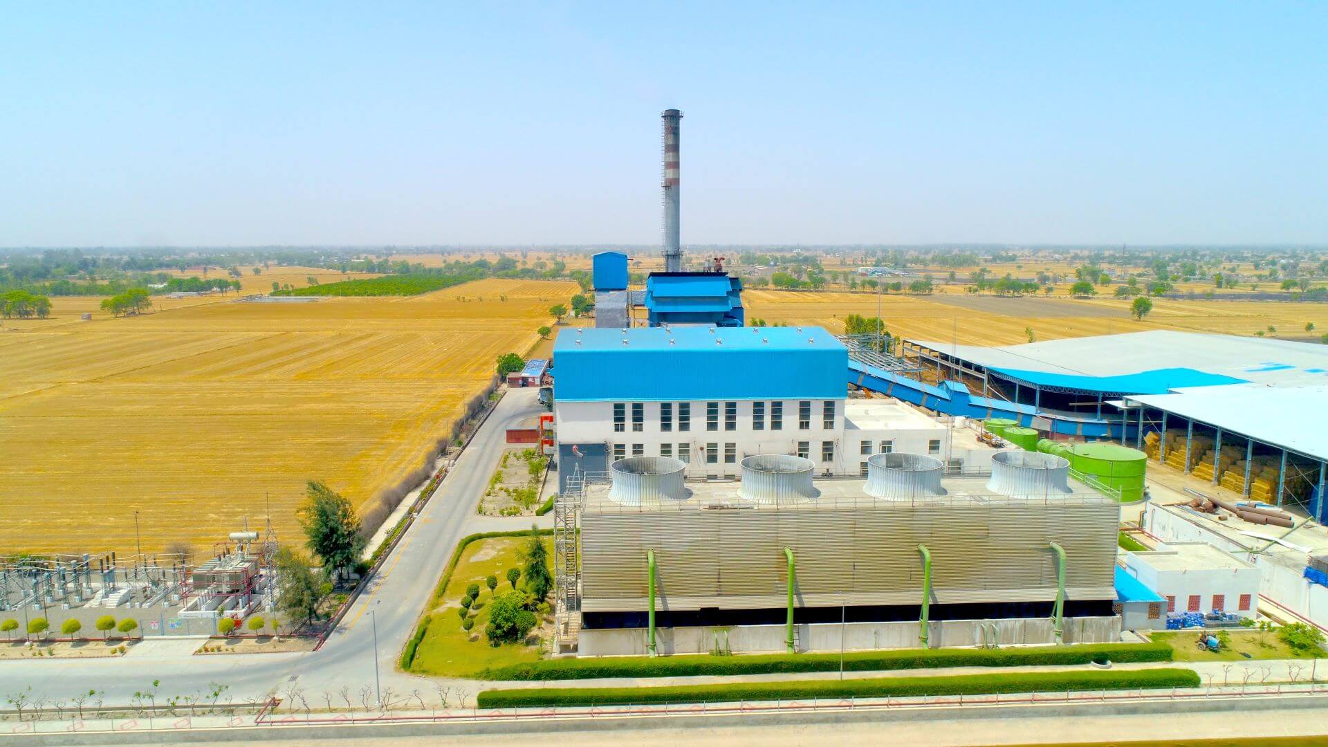 Industrial buildings with blue roofs and with chimney and tanks, with straw coloured fields behind
