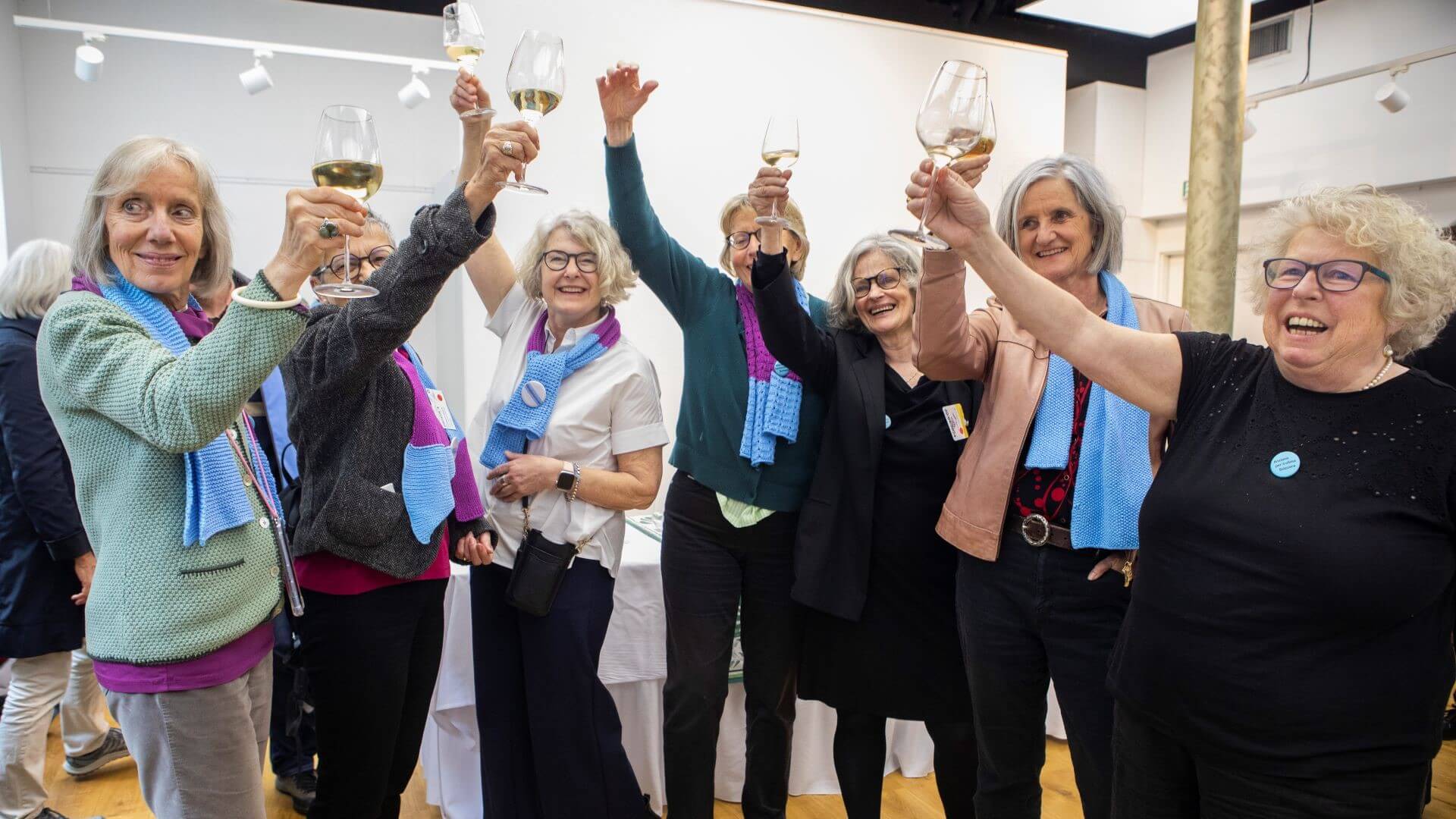 Group of older women smiling and raising wine glasses in the air in celebration