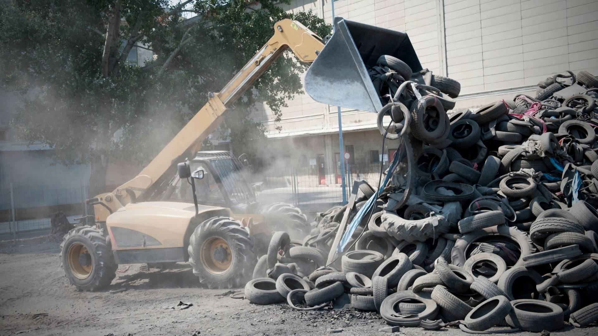 Industrial bucket loading moving large waste rubber tyres into a pile