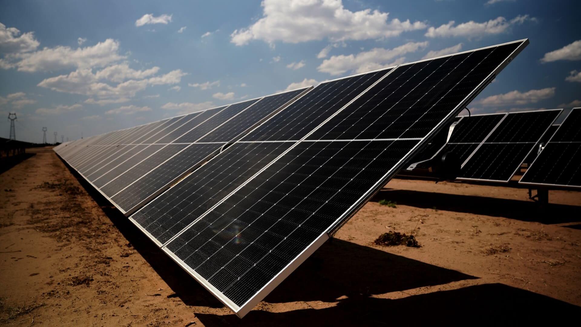 Close up of a row of solar panels on dusty ground, tilted at an angle, facing the sky