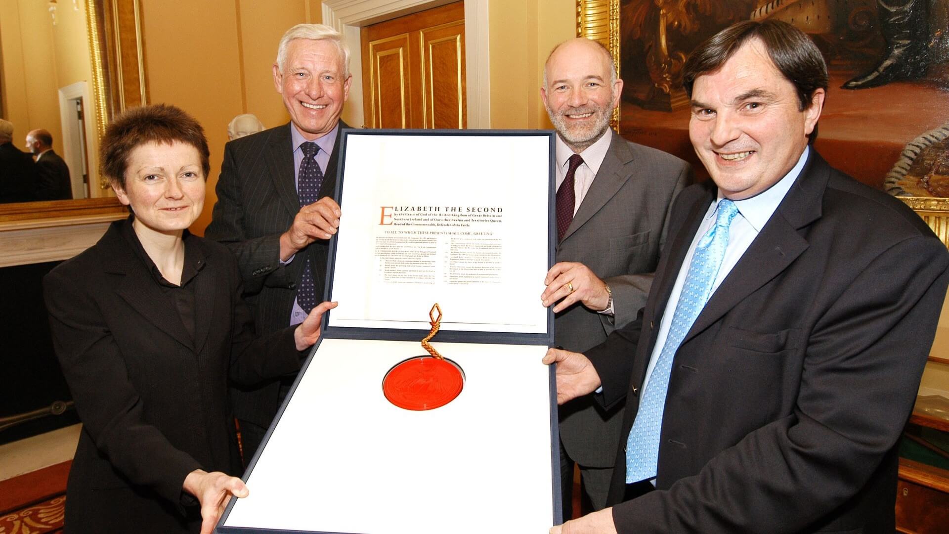 Three men and one woman proudly holding a large framed certificate with official seal
