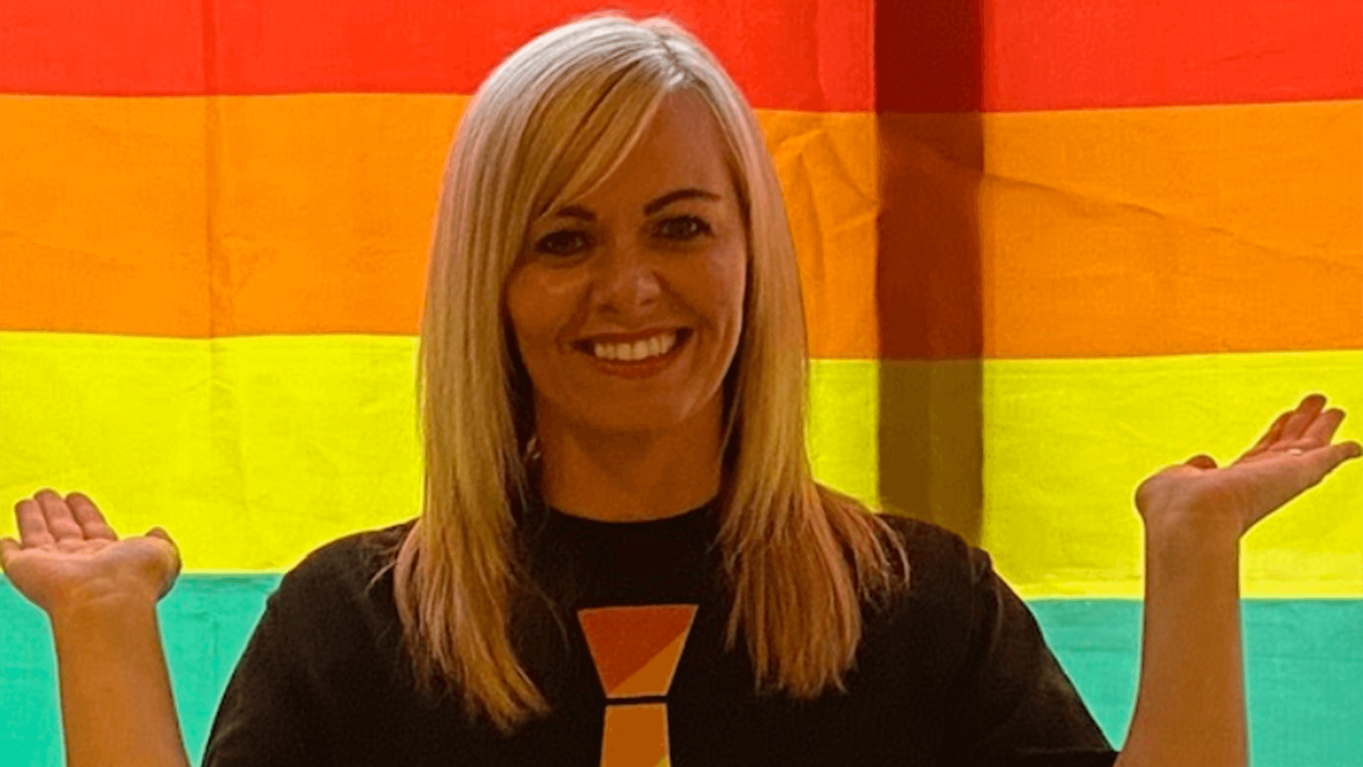 Head and shoulders photo of Louise Bailey, with rainbow Pride flag as backdrop