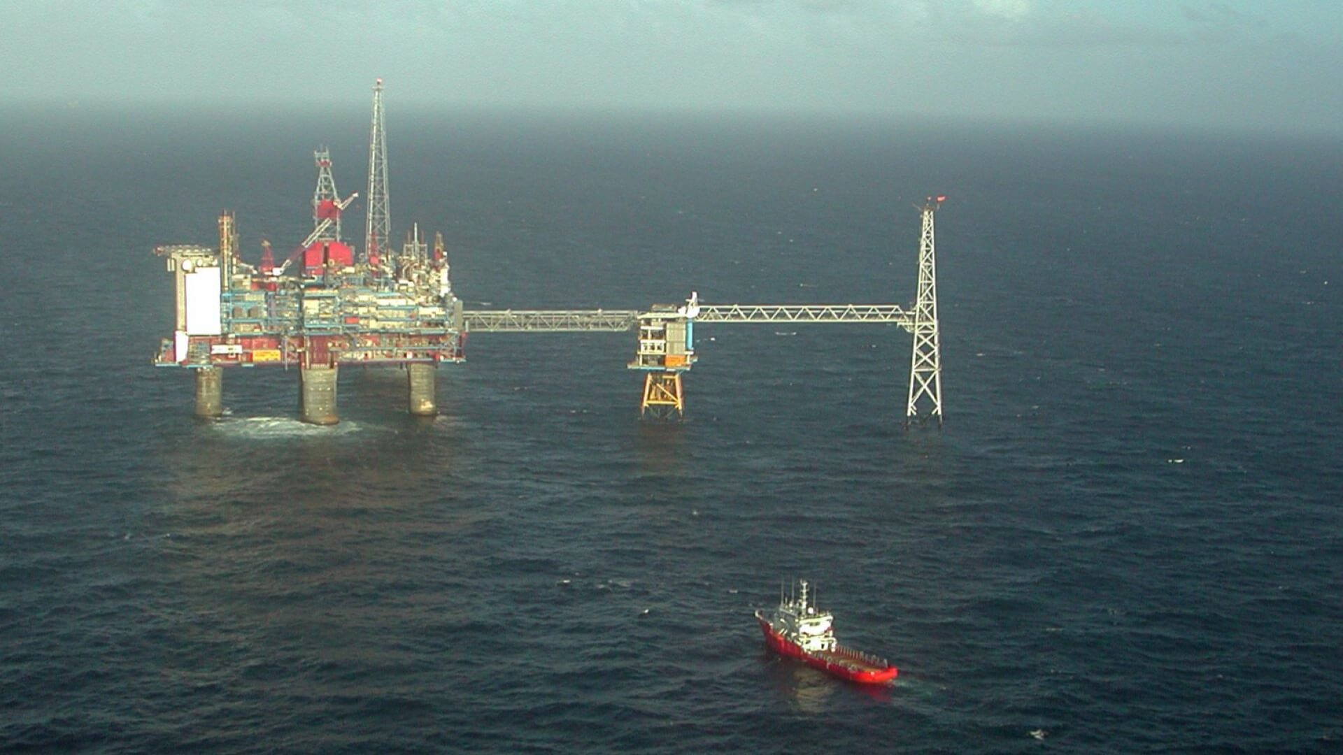 Aerial view over Sleimnir oil platform in calm sea, with a supply vessel approaching in foreground