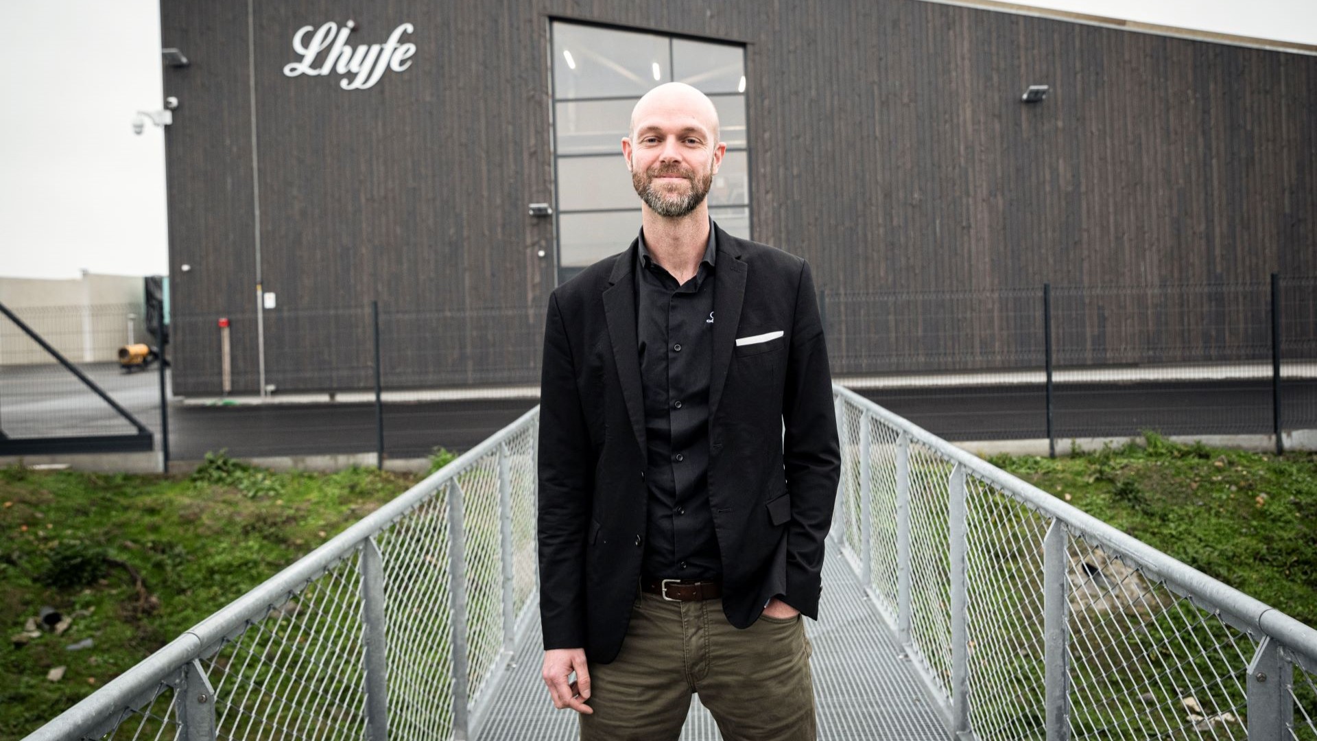 Matthieu Guesné, Founder and CEO of Lhyfe, standing on handrailed walkway leading to modern building with Lhyfe logo on side