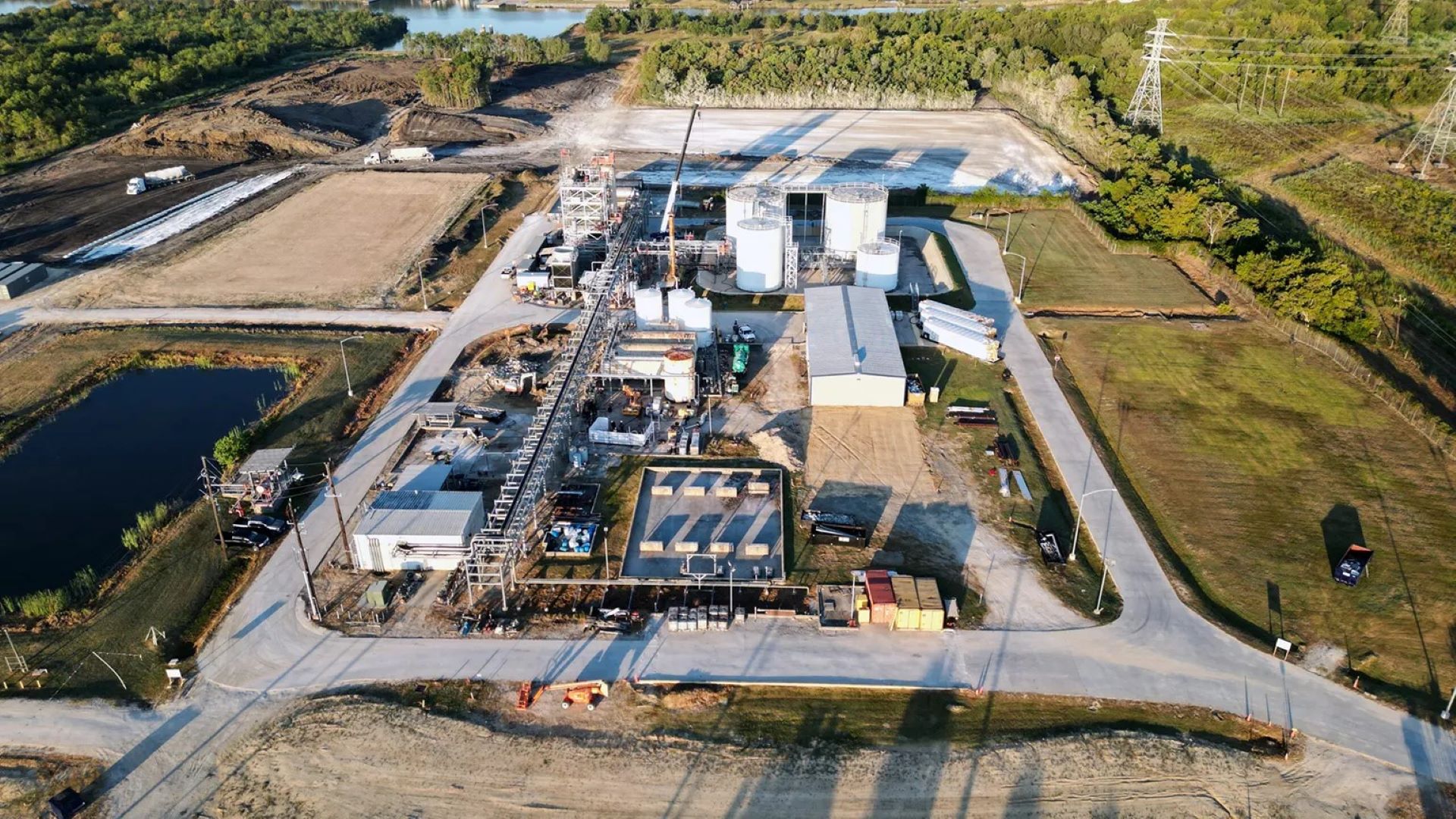 Aerial overview of industrial plant with storage tanks, green fields to side
