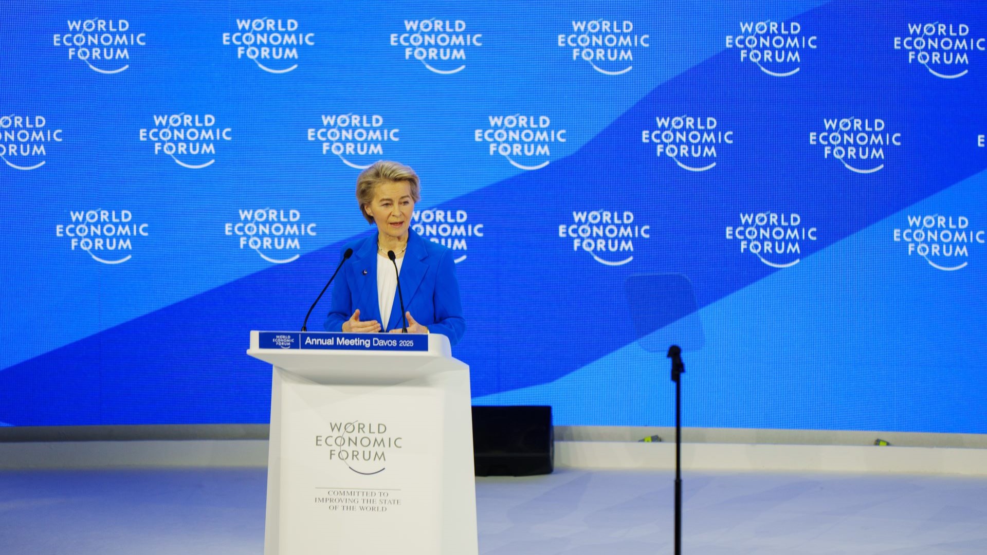 Ursula von der Leyen, President of the European Commission, standing behind lectern on stage, with World Economic Forum logos on large blue screen behind