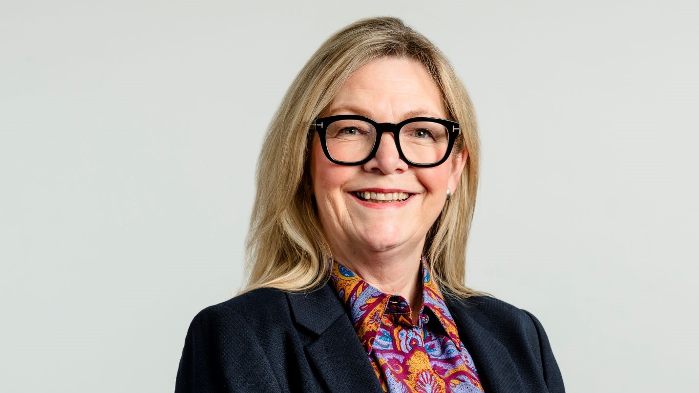 Head and shoulders photo of woman wearing glasses, against grey backdrop
