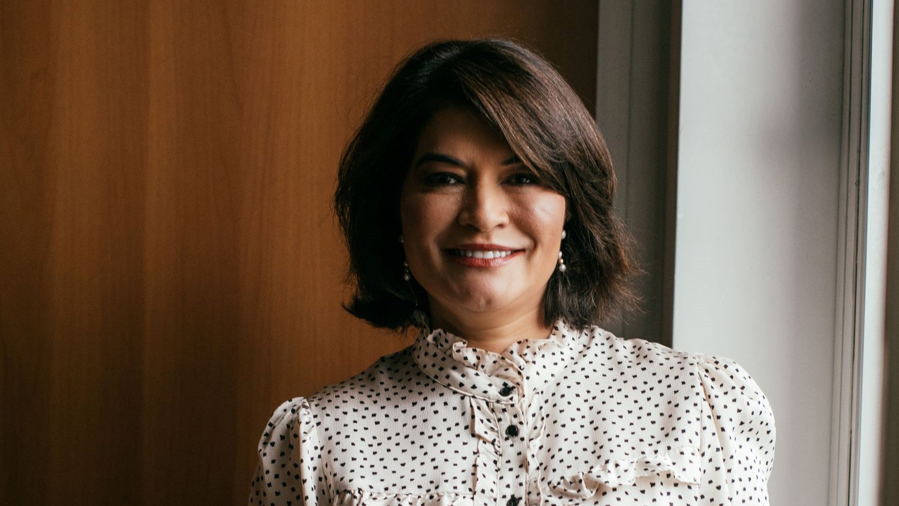 Head and shoulders photo of Elbia Gannoum, standing in front of closed office door and by a window