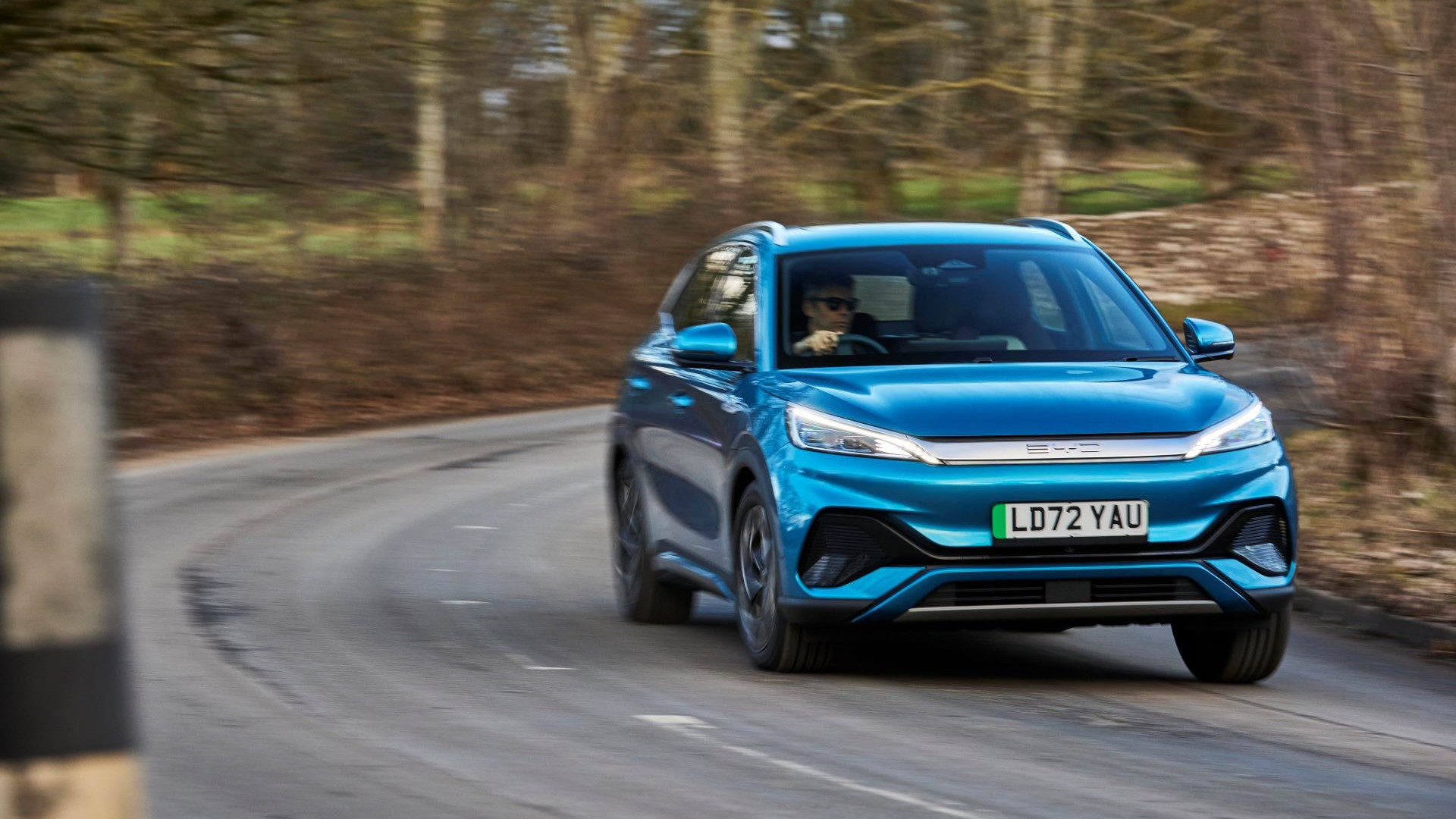 Blue electric car driving round bend of countryside road