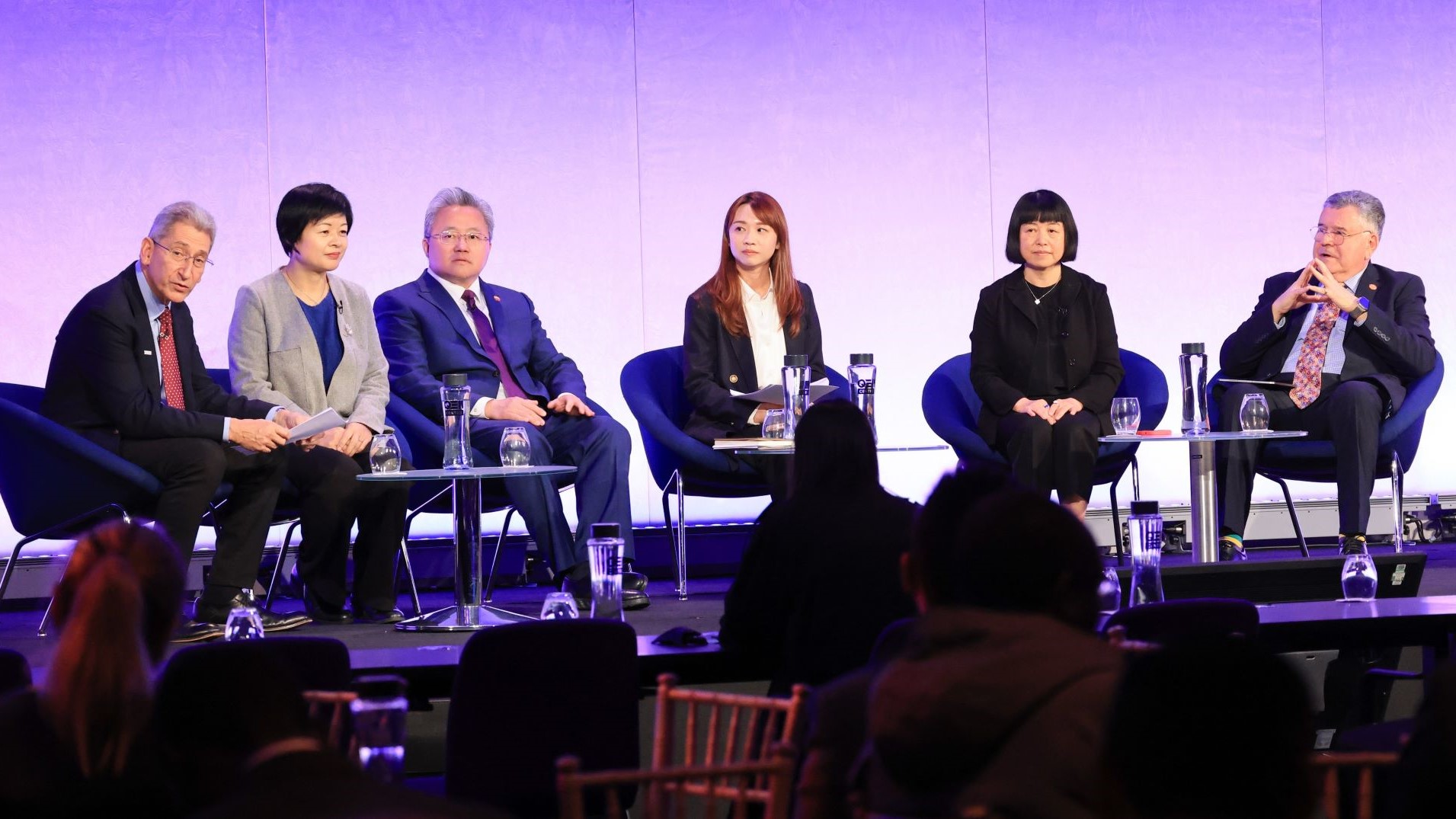 Row of panel speakers sitting on chairs on stage - 3 men and 4 women - talking to conference delegates
