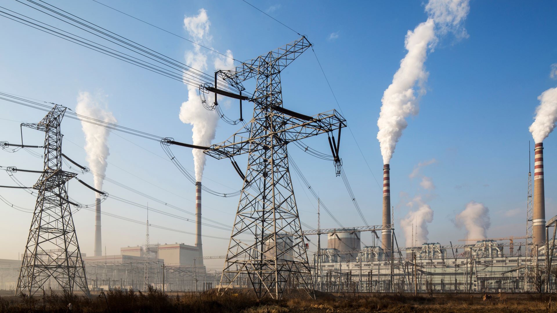 Coal-fired power station with smoke rising from chimneys and pylons in foreground
