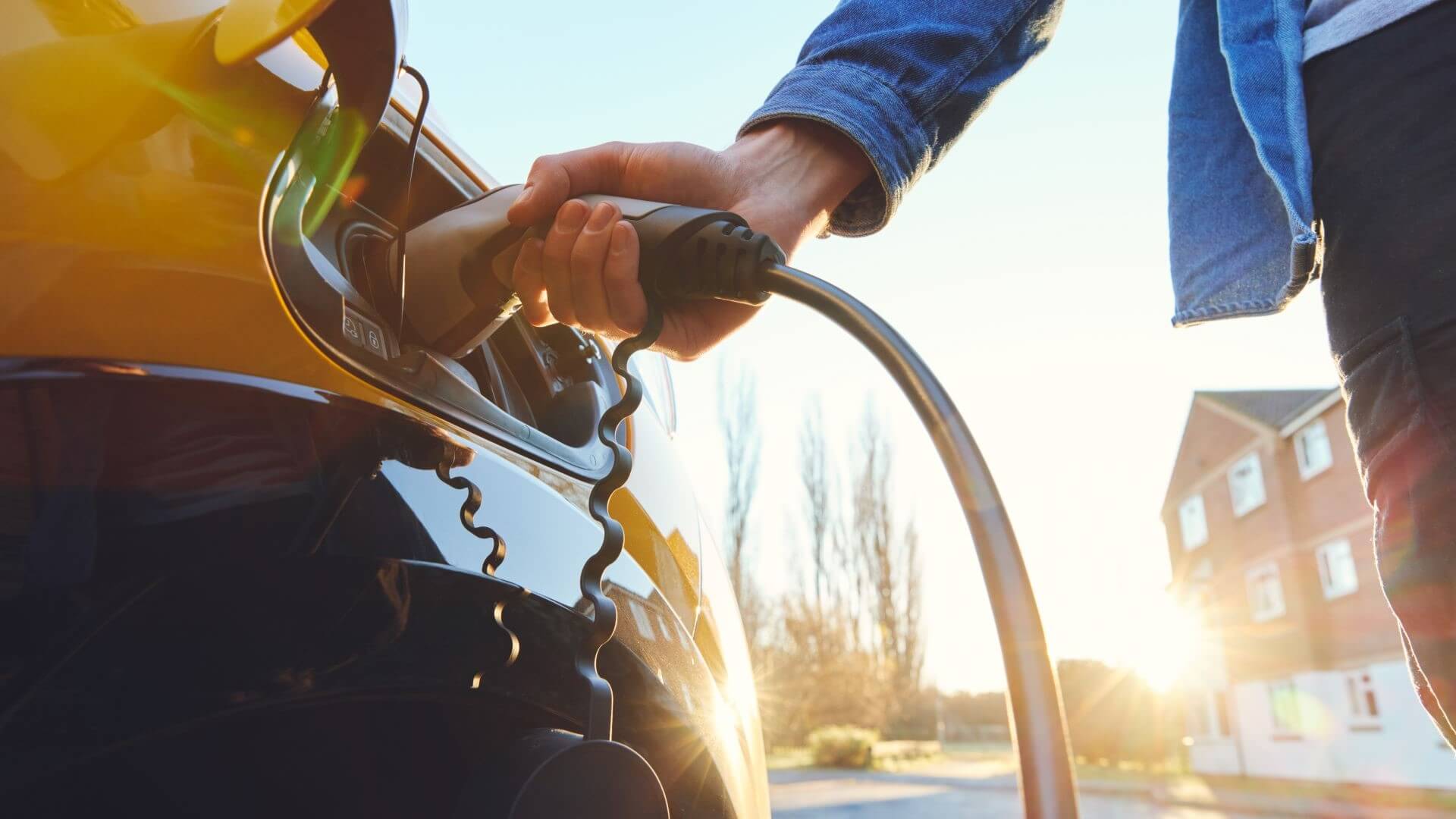 A person plugging in a charger to an electric vehicle outside a house