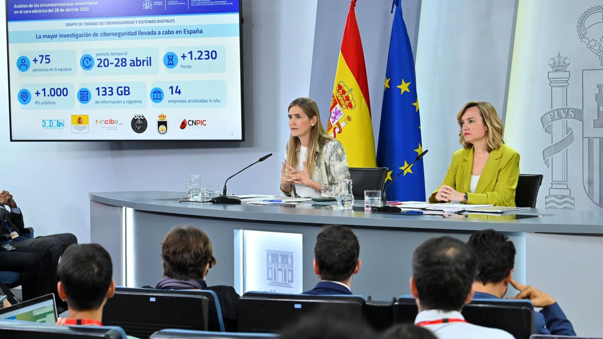 Two women behind desk addressing a crowd of people