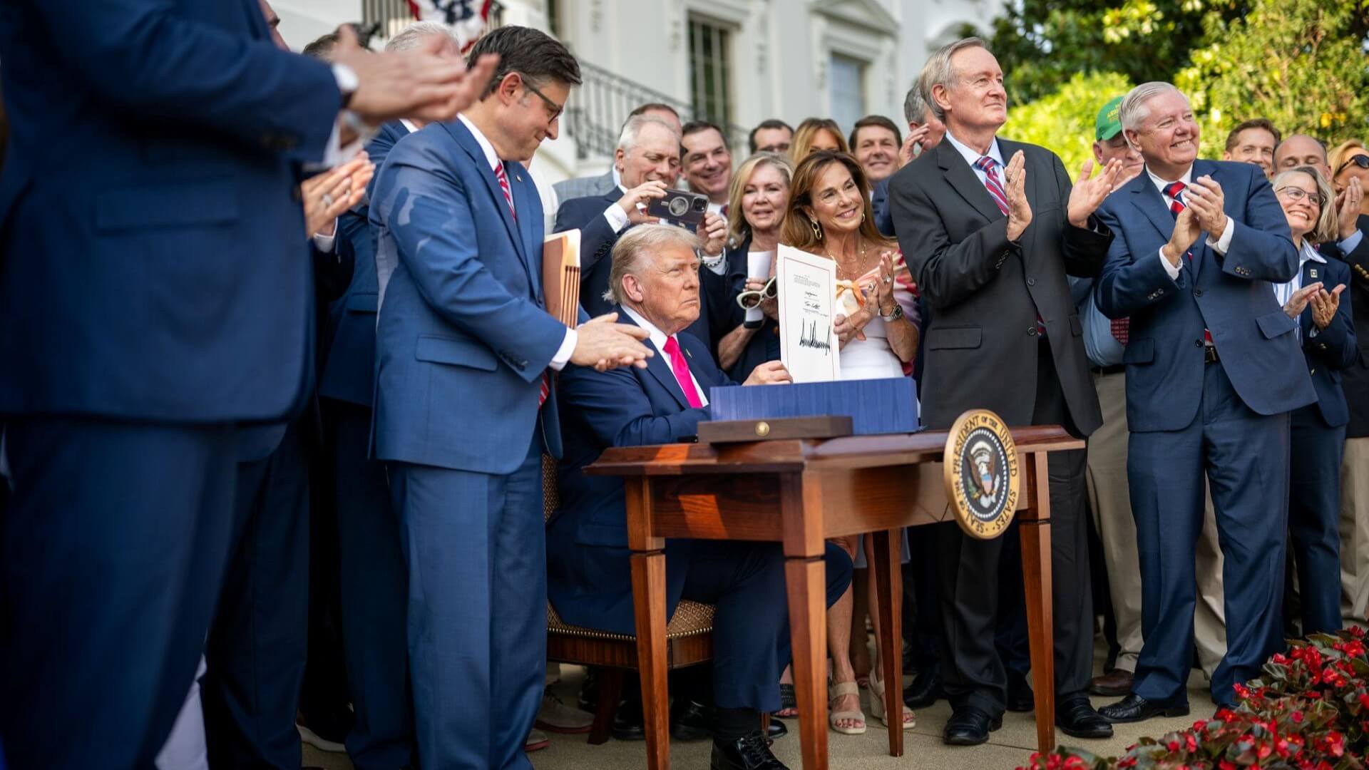 US President Donald Trump at desk surrounded by group of people