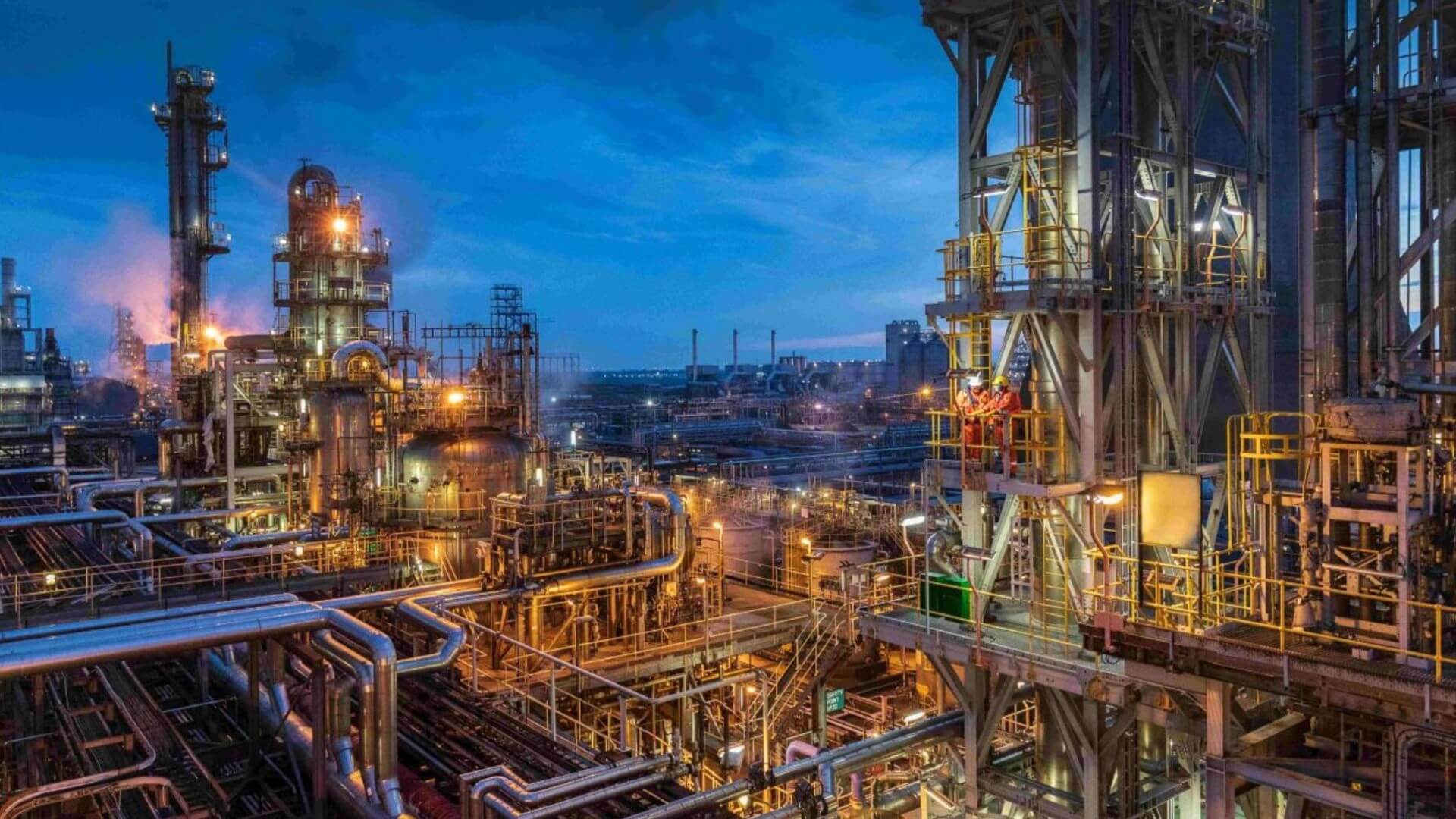 Aerial overview of towers and pipework at an industrial plant, lit up at night