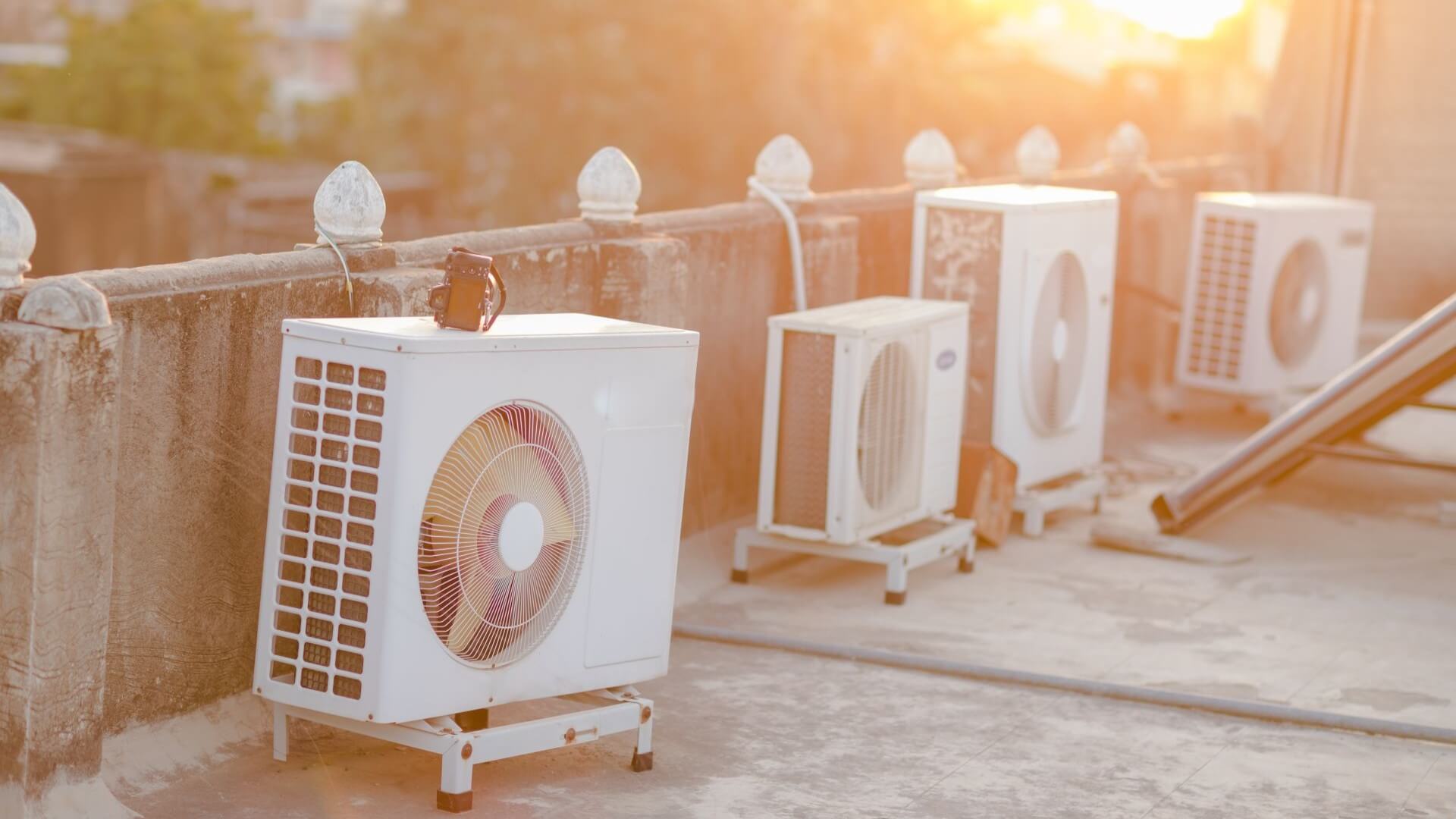 Row of four air conditioning units on building rooftop, with sun shining in background