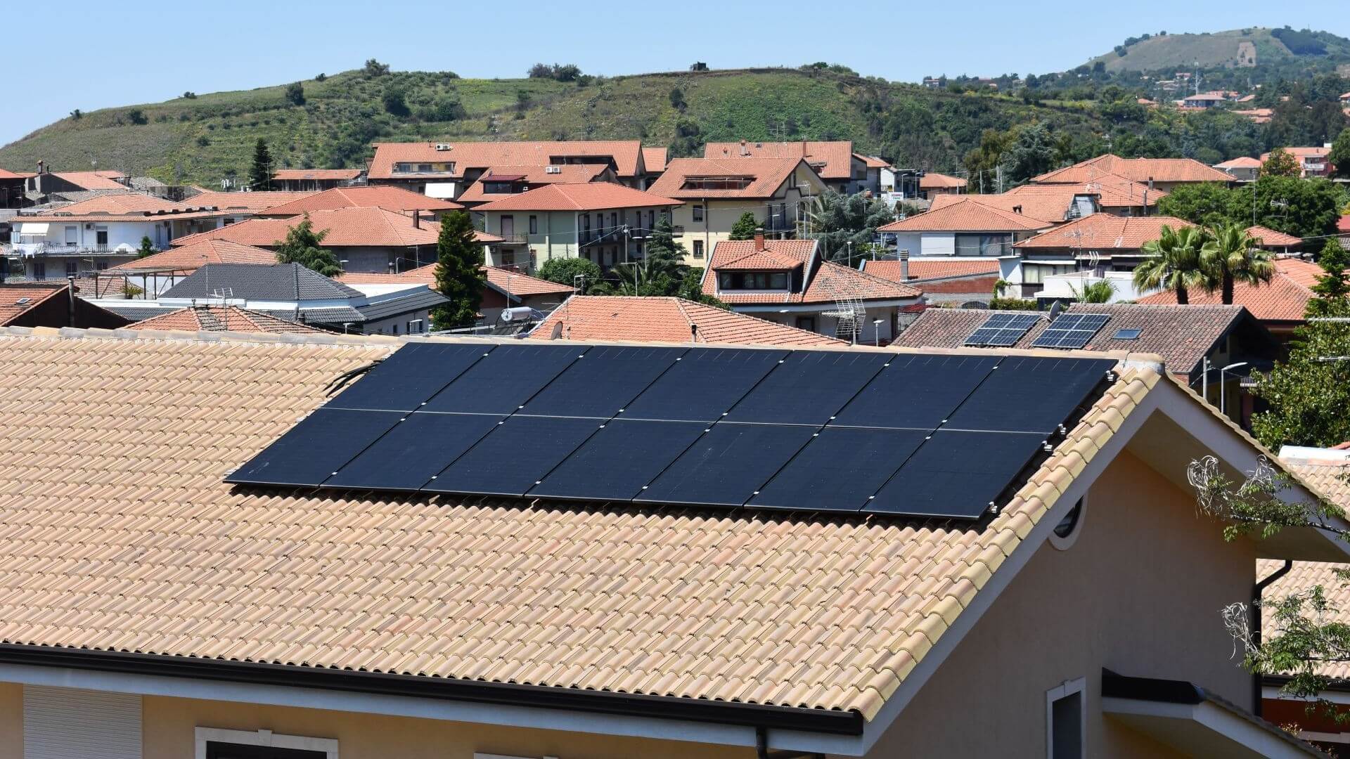 View over orange tiles of residential rooftops with building in foreground fitted with a few solar panels