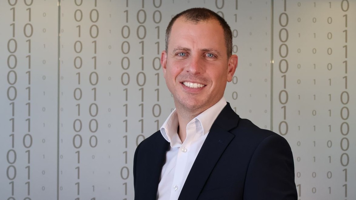 Head and shoulders photo of man standing against a white background filled with columns of binary numbers, zeros and ones
