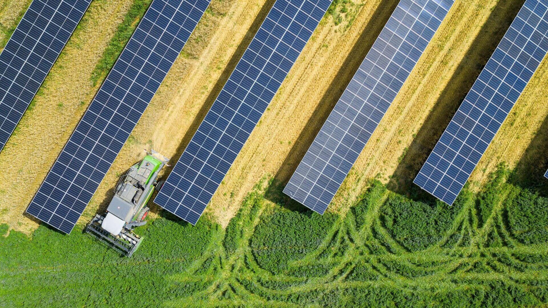 Aerial view of farming machinery working in between rows of solar panels
