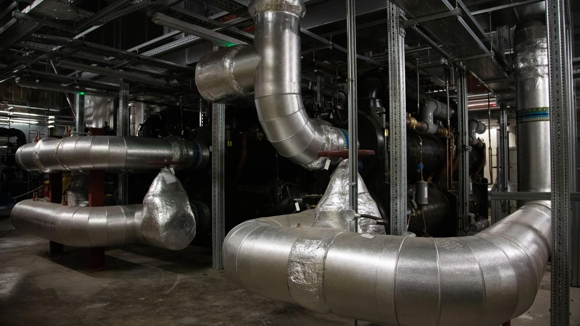 Big dark silver piping forming part of heat pump installation in basement of building