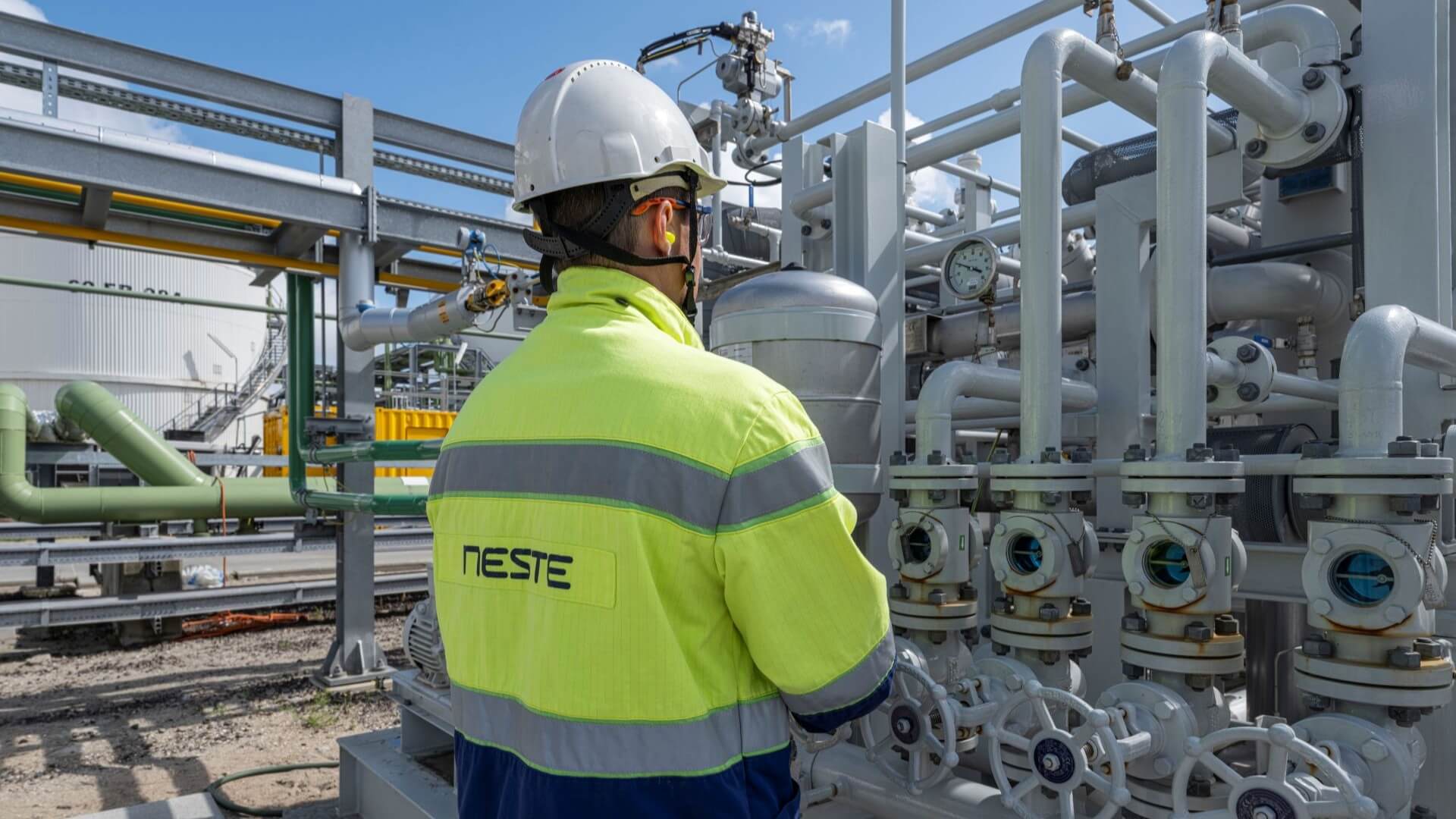 A person in a safety jacket and white helmet at a refinery