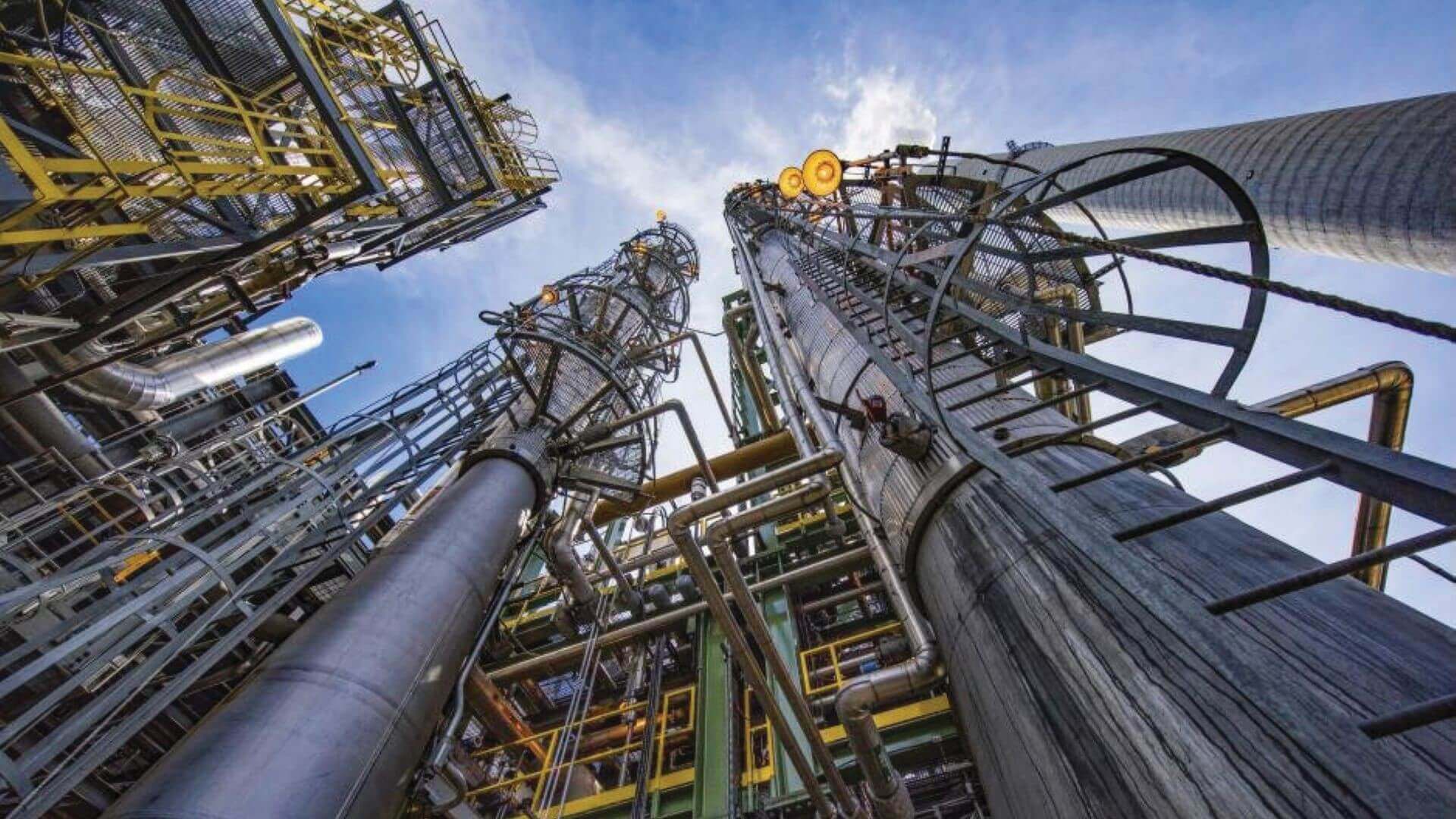 View looking up grey and yellow pipeline of carbon capture plant to see blue sky and white clouds above