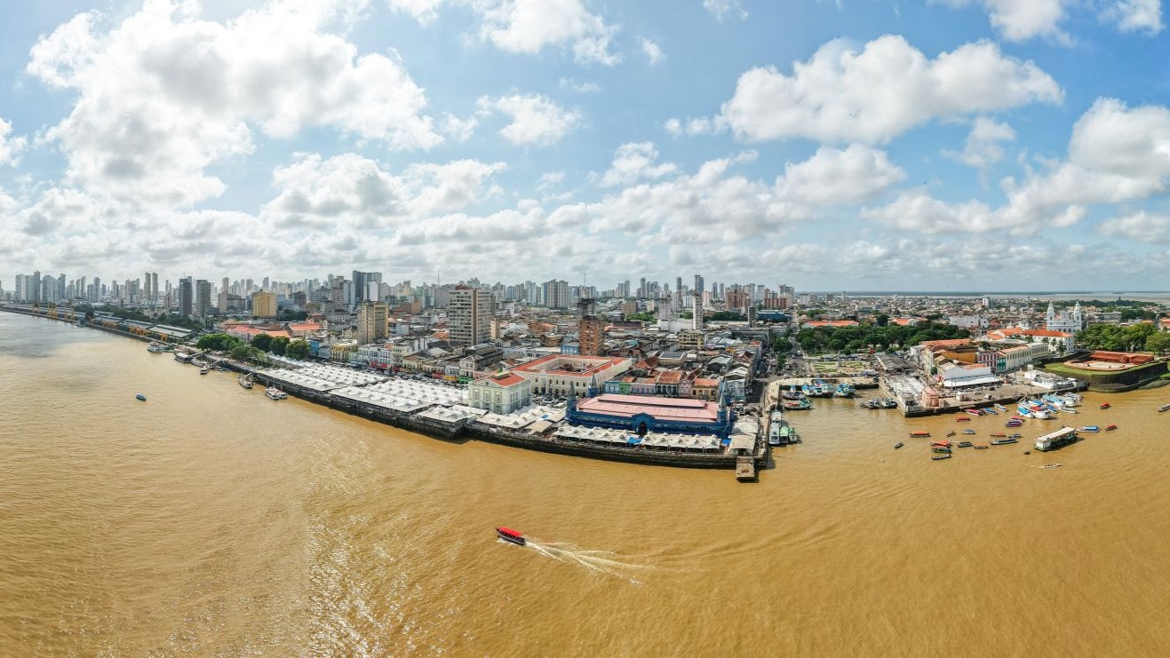 Overview of city of Belém, from the air, looking from above the sea to land, showing skyscrapers and other city buildings as well as small boats just offshore