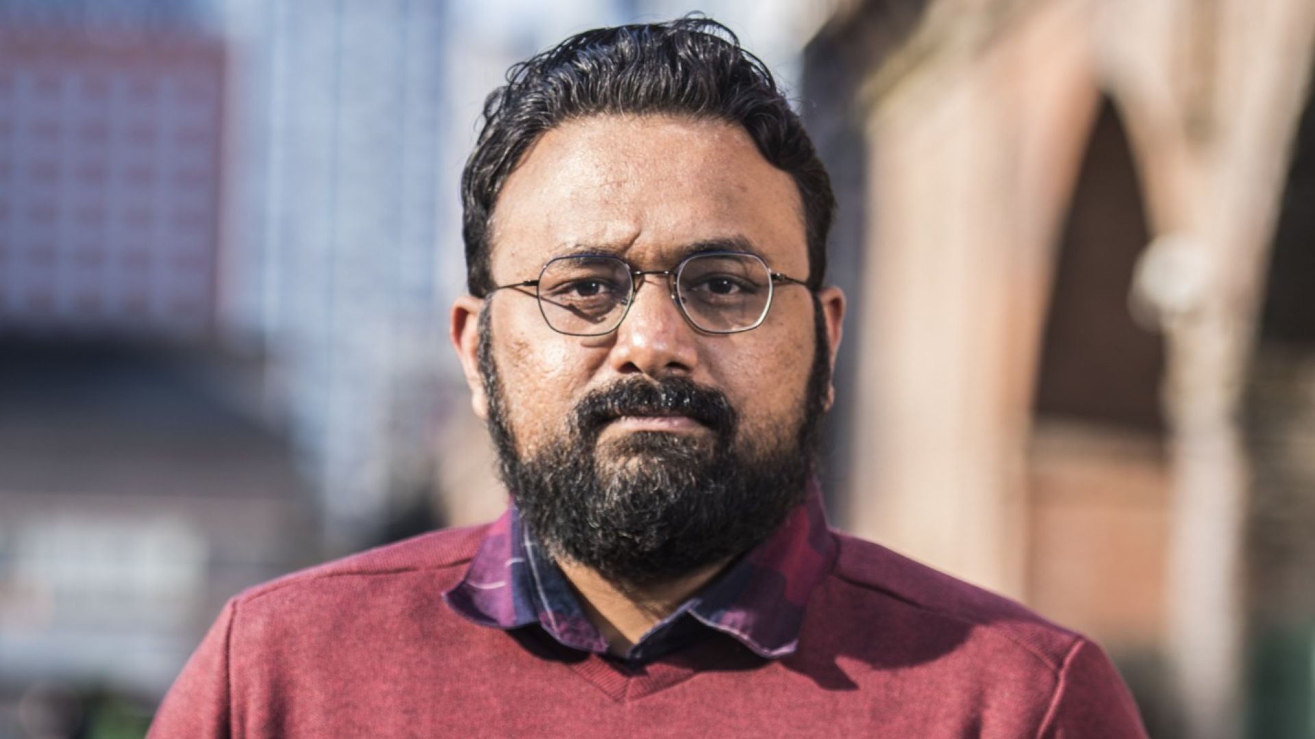 Head and shoulders photo of Gaurav Gharde, standing in front of a modern building and arches of an older building, both faded out