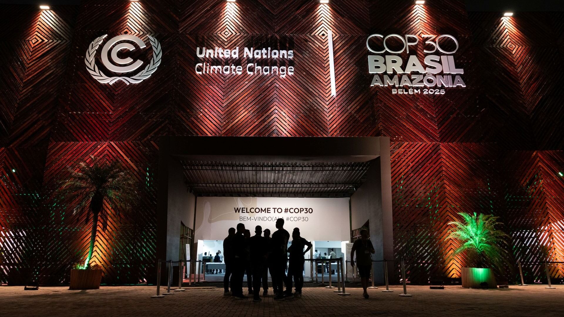 Silhouette of a group of people standing in front of dimly lit COP30 stage