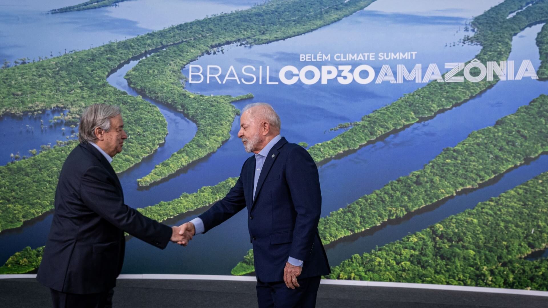 Two men shaking hands on stage, standing in front of screen showing photo of meandering river and forest