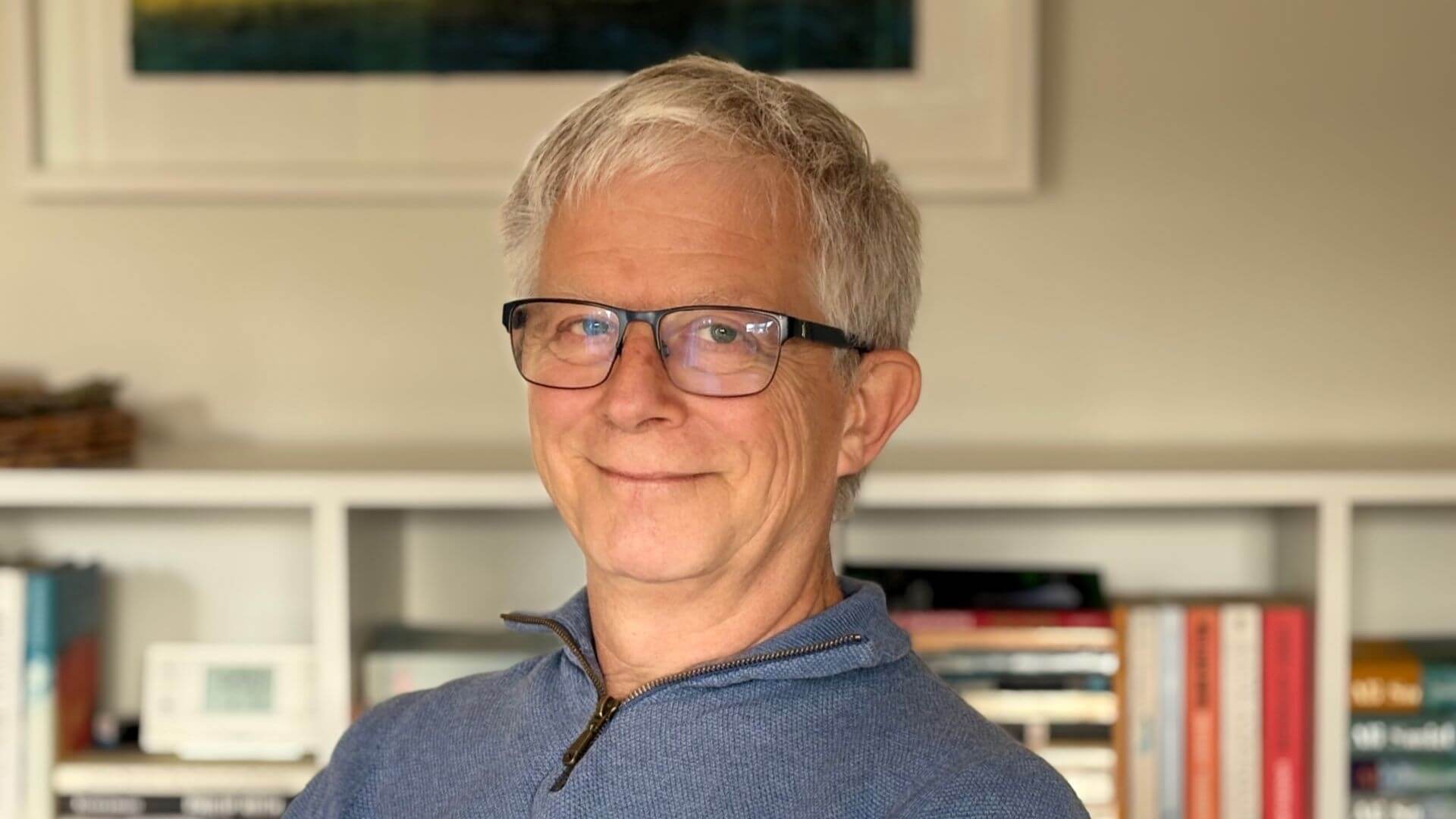 Head and shoulders photo of Tony Day with picture on wall and bookshelf with books in background
