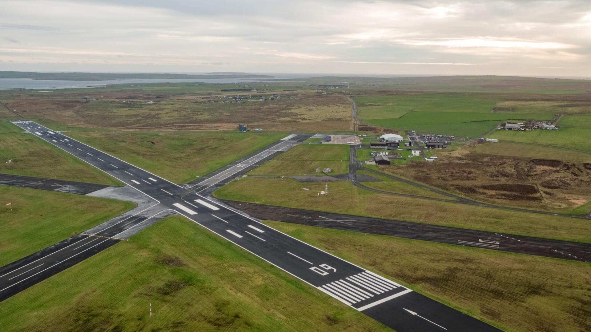 Aerial view over small airport showing the X-shape of two crossing runways and small airport buildings set among green fields