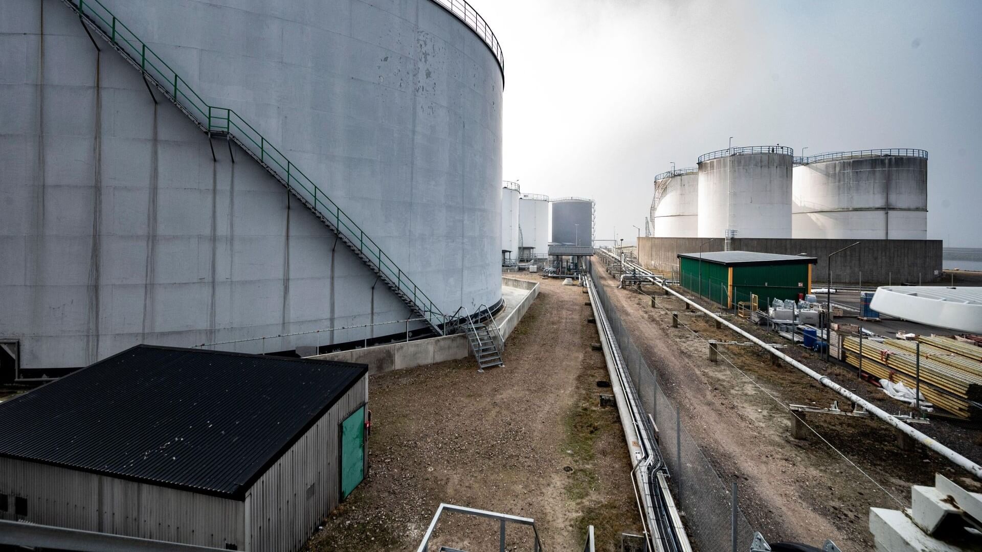 Cylindrical bulk storage tank in foreground on left of photo, with pipes running to right and into distance, where a number of other storage tanks can be seen
