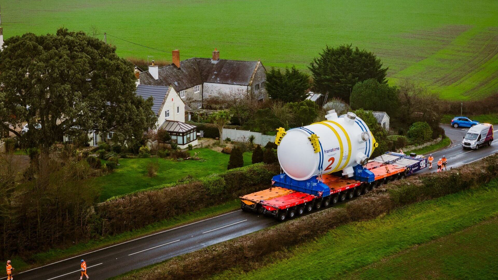 Aerial view of nuclear reactor being transported by road with surrounding houses