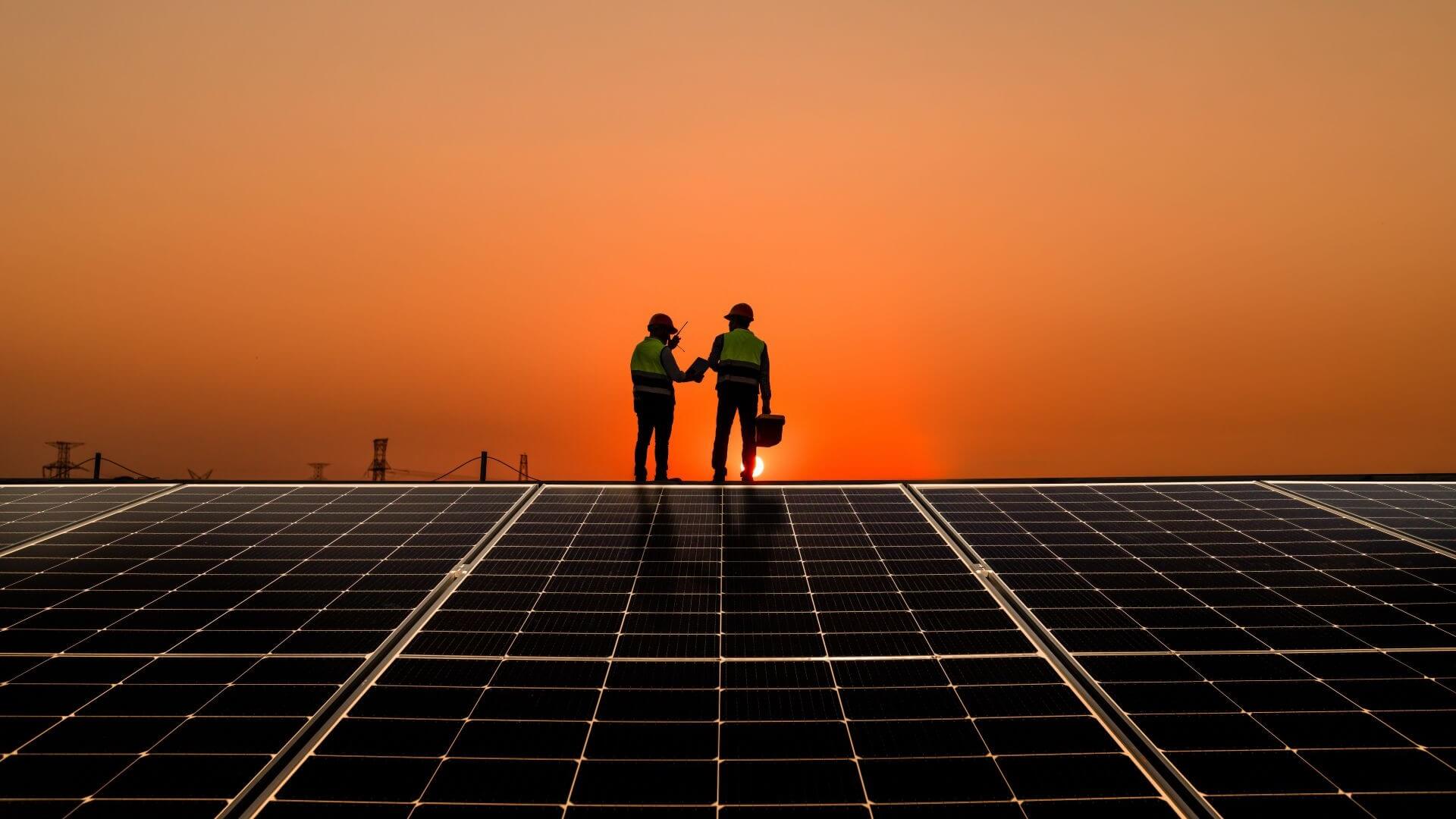 Silhouette of two engineers working near solar panels at sunset