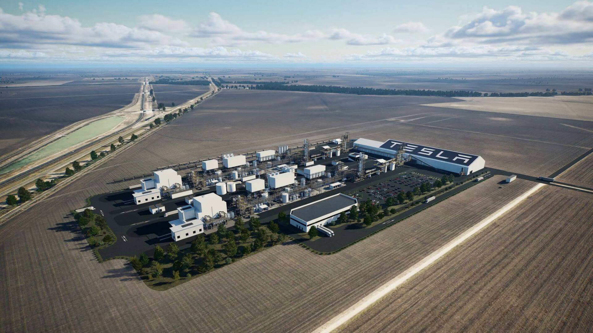 Aerial view over industrial facility, with many rectangular buildings and cylindrical tanks - one large building has Tesla written on the roof