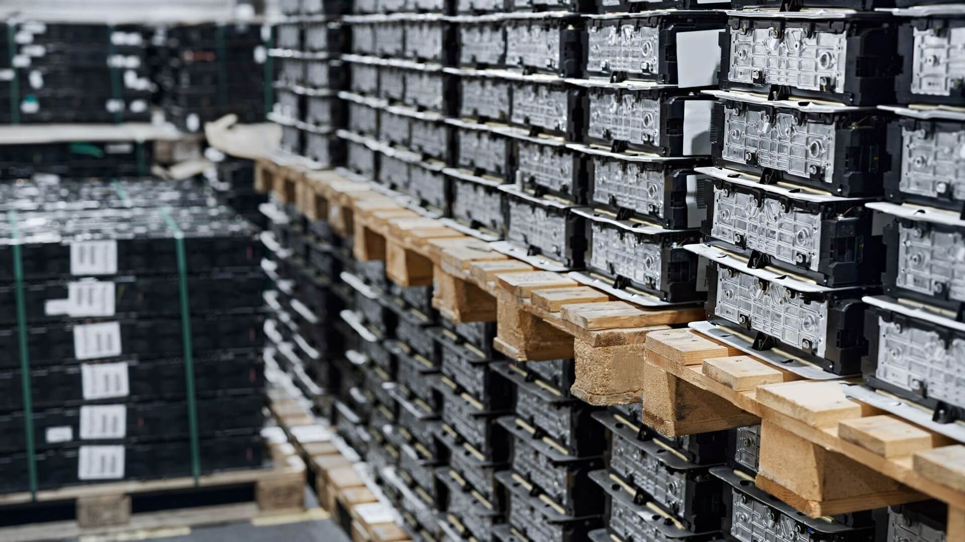 Row upon row of rectangular black lithium ion batteries stacked upon one another, on wooden pallets 