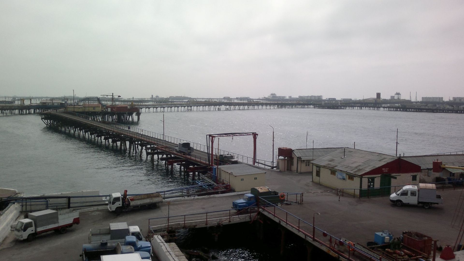 Network of criss-crossing jetties on wooden supports over calm water, with small trucks in foreground and low buildings