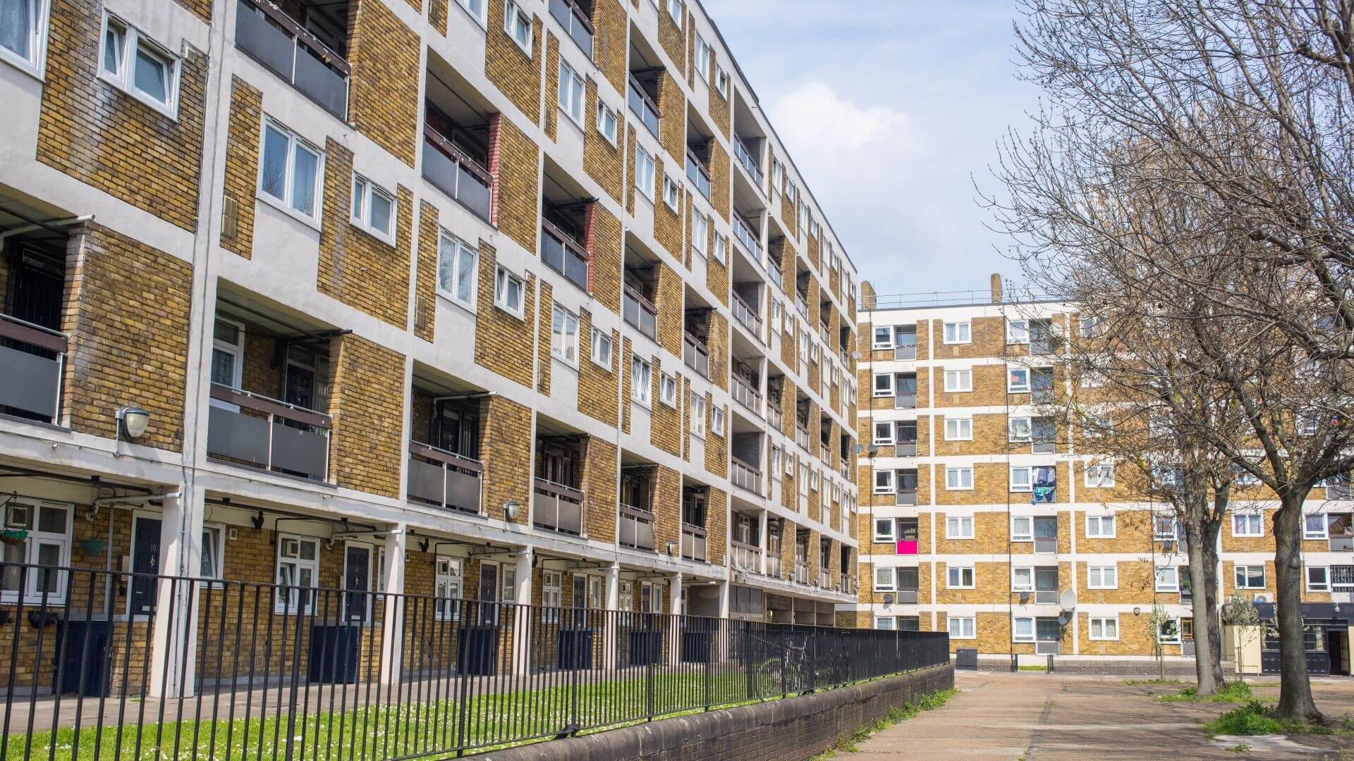 Looking along the side of apartment building, with lots of windows and balconies, with another block face on in the backgroud