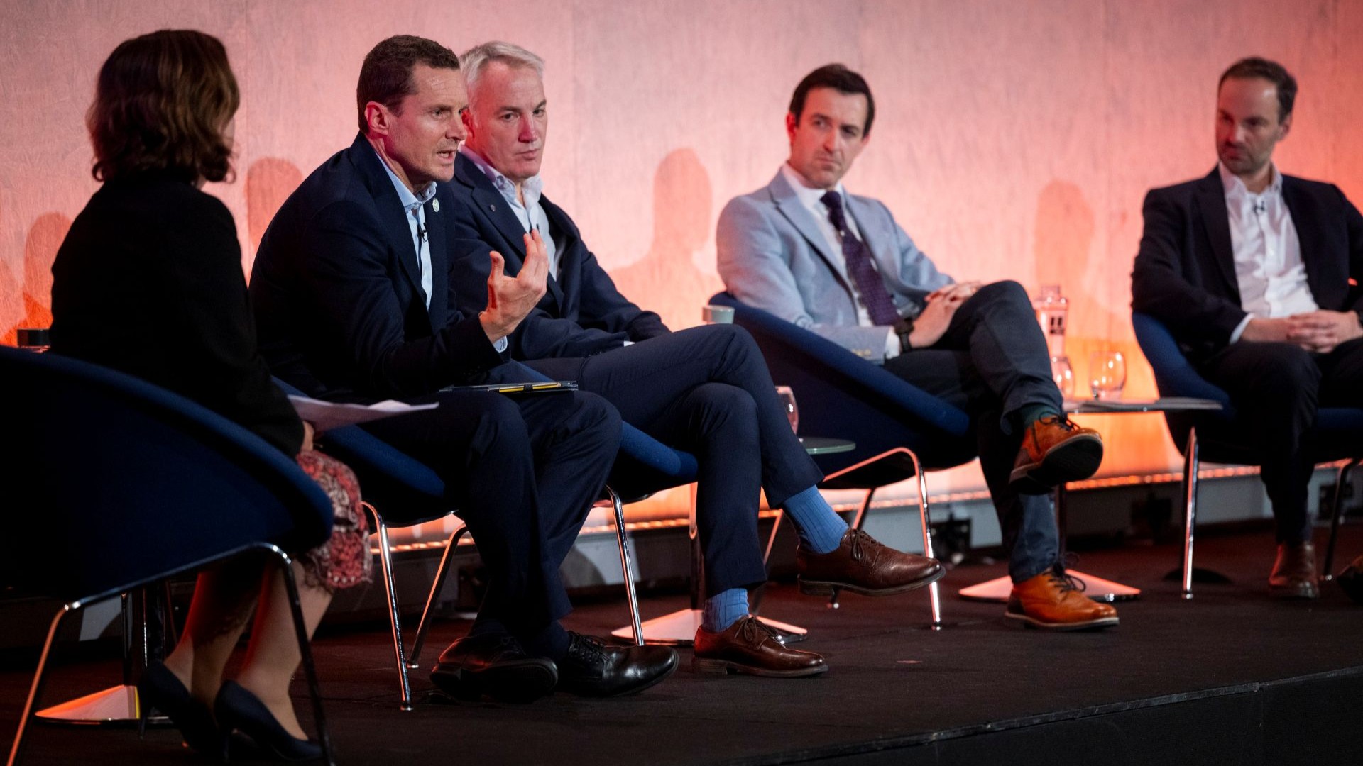 Five panellists sitting in chairs on conference stage, talking and listening to one another