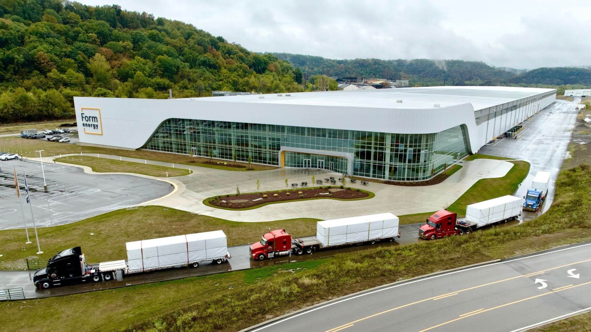 Aerial view showing four trucks carrying batteries leaving a factory