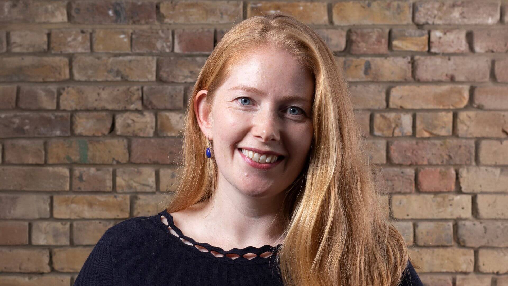 Head and shoulders photo of Jo Alexander, standing in front of a brick wall
