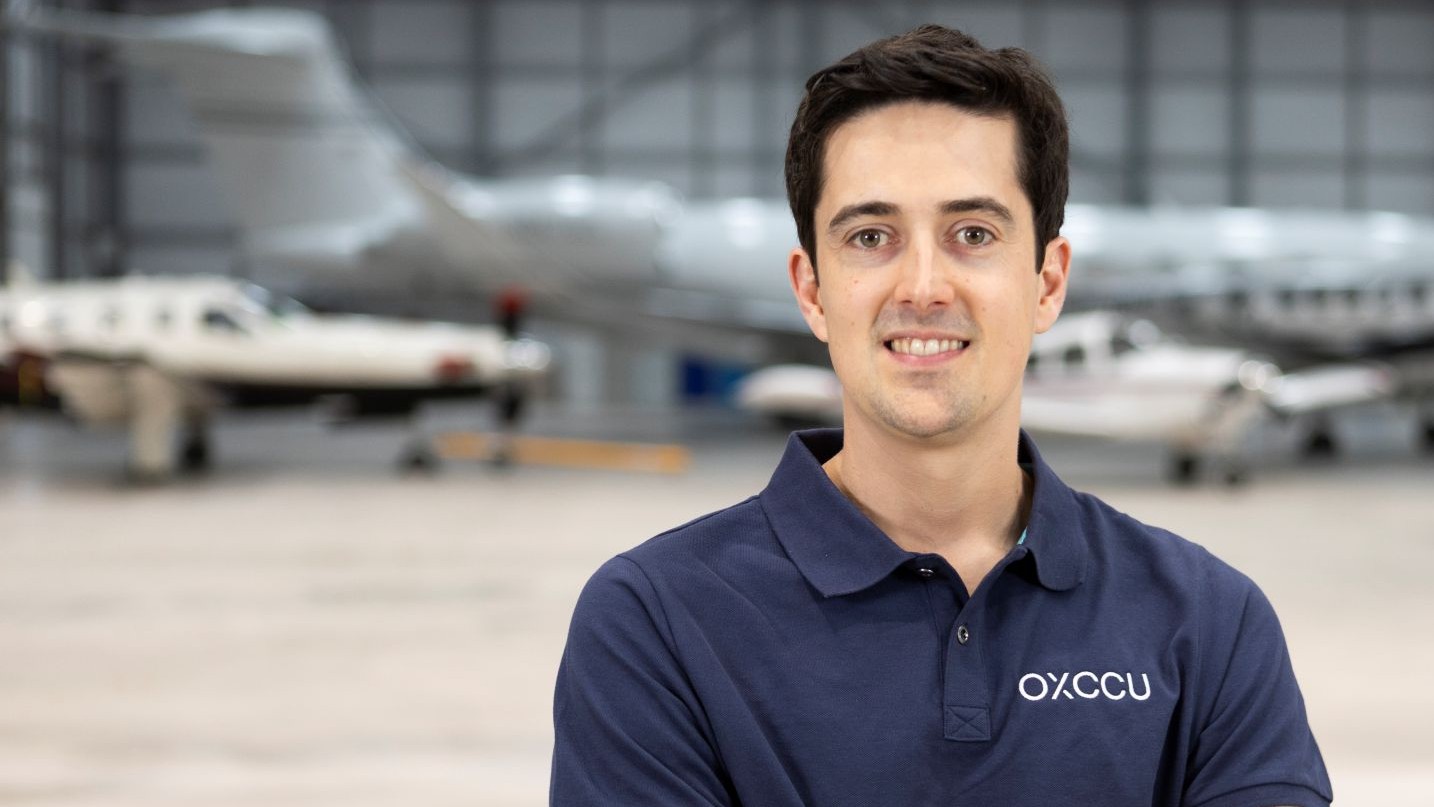 Head and shoulders photo of Andrew Symes, with blurred small aircraft in the background